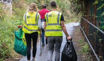 Two people walking in high-vis jackets with litterpicking gear
