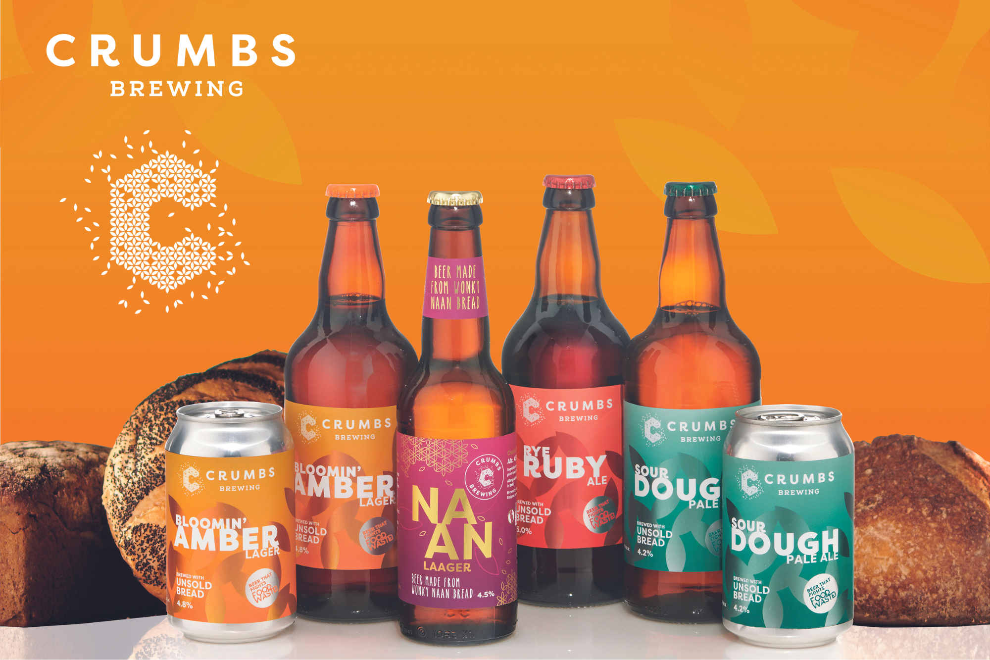 Image of 3 bottles and 2 cans of beer made by sustainable craft brewery, Crumbs Brewing. Bottles and can are on a flat surface against an orange background with loaves of bread behind them