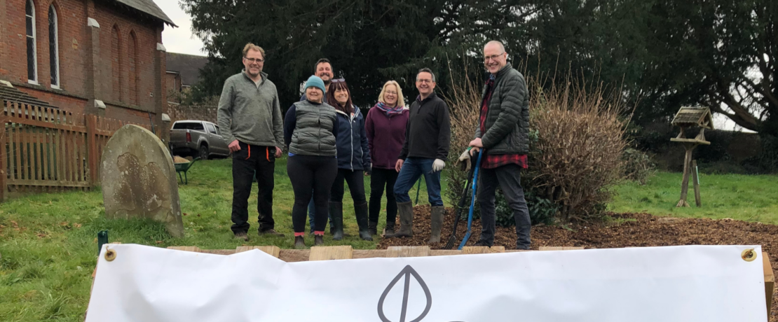Image of Green Westcott Community Garden, with white sign at the front of image and view of the garden with volunteers in the background
