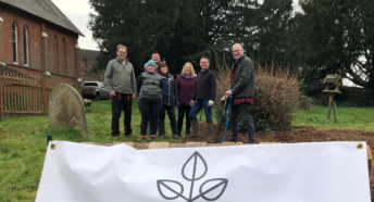 Image of Green Westcott Community Garden, with white sign at the front of image and view of the garden with volunteers in the background