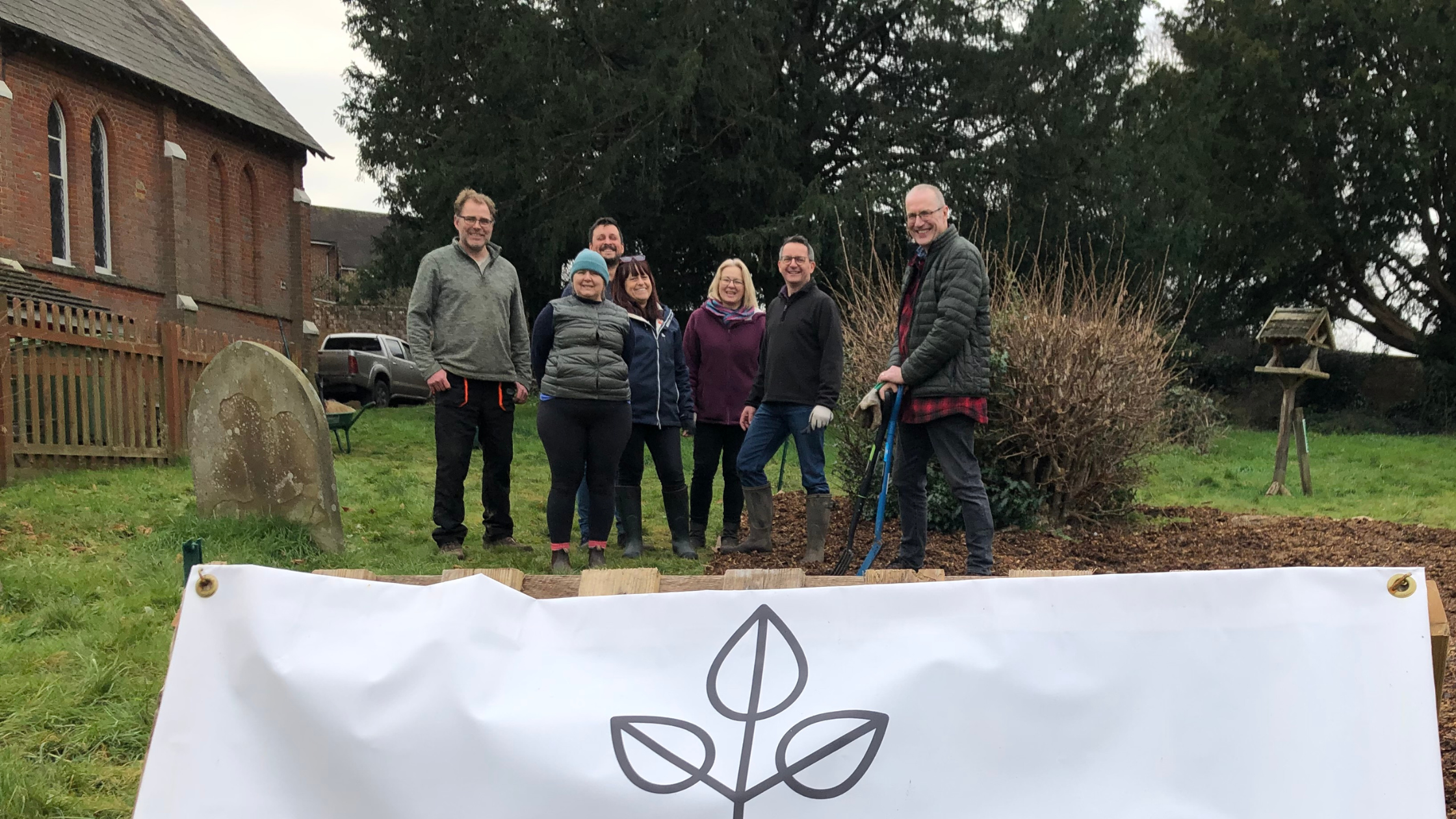 Image of Green Westcott Community Garden, with white sign at the front of image and view of the garden with volunteers in the background