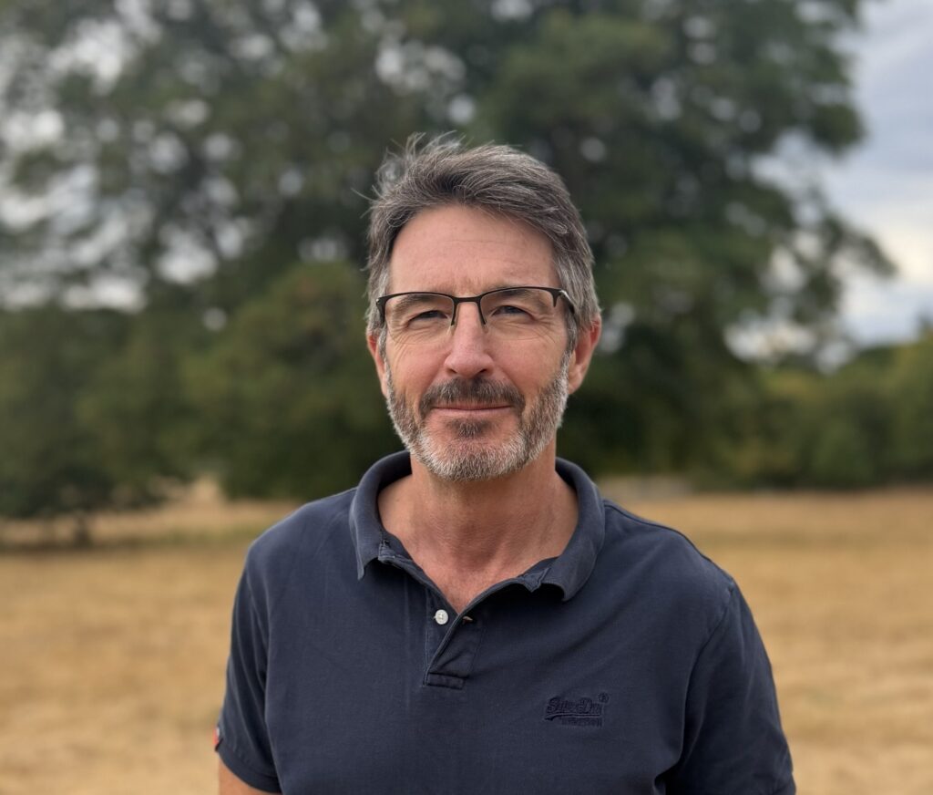 Image of trustee Rob Crossing against the backdrop of a field with trees and hedges in the background