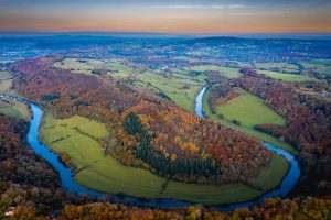 A view over a winding river curving through a green landscape with autumn colours in trees