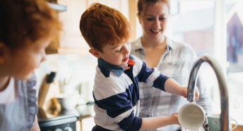 Child helps mother wash up at the sink