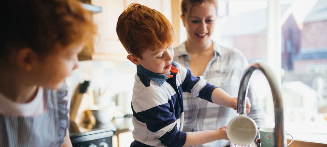 Child helps mother wash up at the sink