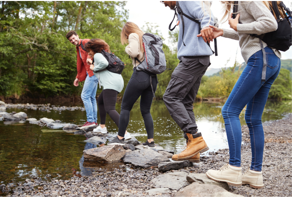 Five young people cross stepping stones across a stream