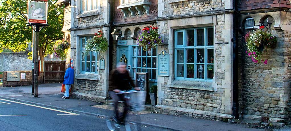 A man on a bike moves past a pub in pale stone