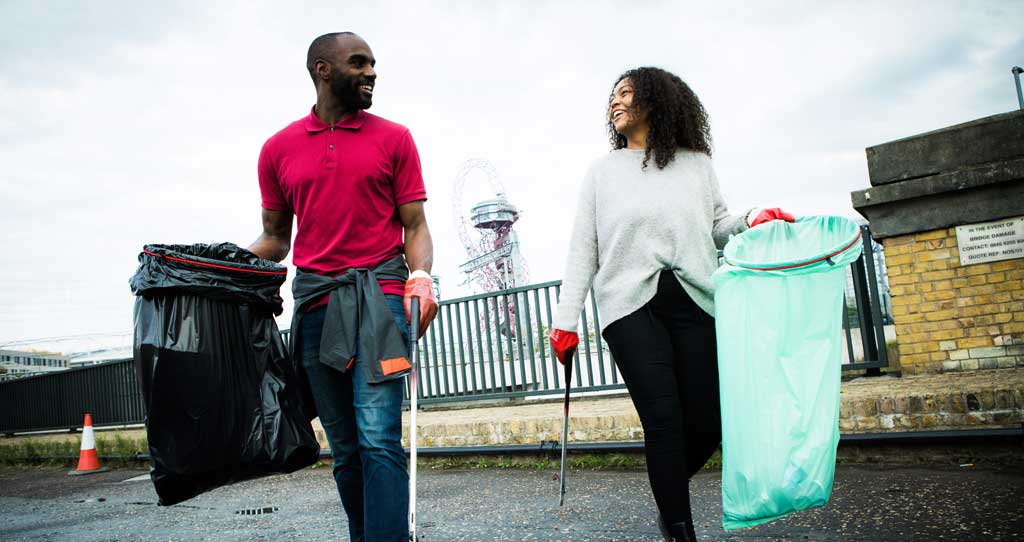 A man and woman with plastic bags and litter pickers in front of London Olympic Park