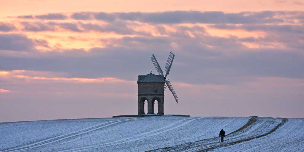 A windmill on a snowy hill at sunset