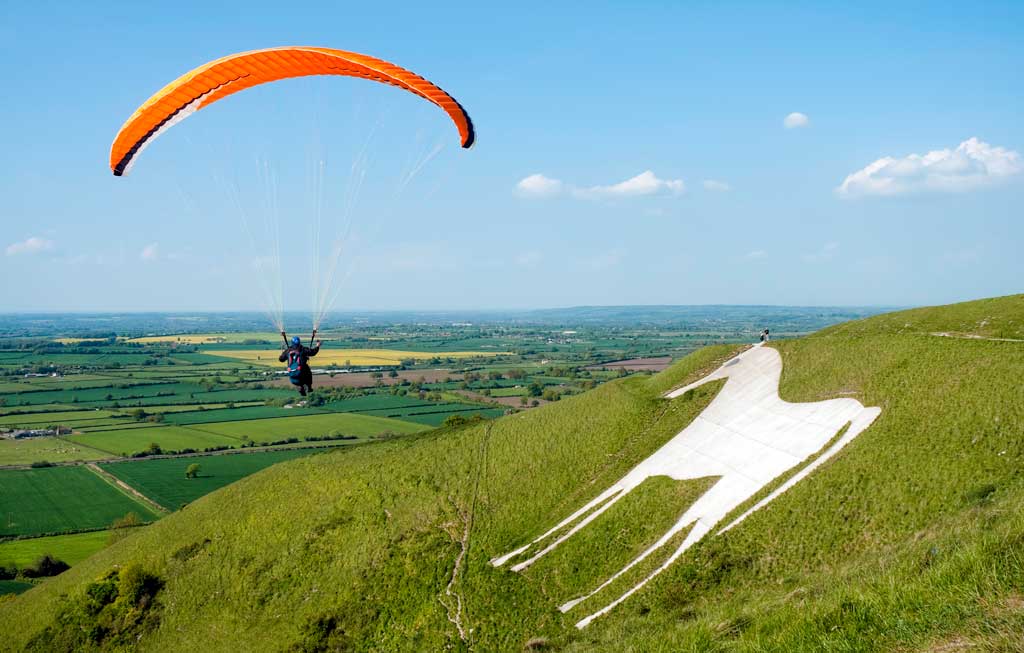 A paraglider with a bright sail flies near to a hill with a chalk horse shape