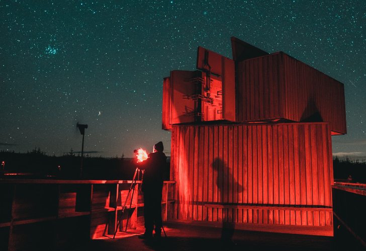A wooden clad building is lit in a red light and starry skies are visible behind