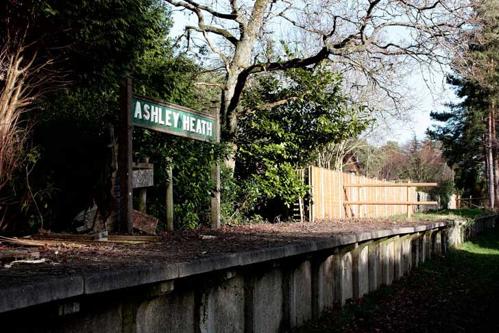 An empty and overgrown train platform with an old fashioned railway station sign visible