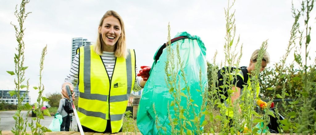 A young woman looks to the camera as she holds a litter picker and rubbish bag