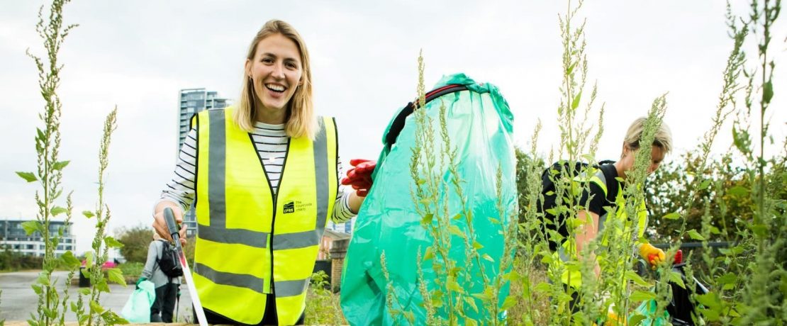 A young woman looks to the camera as she holds a litter picker and rubbish bag