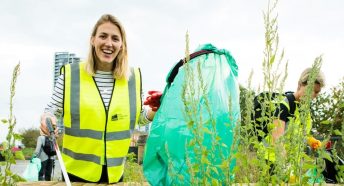 A young woman looks to the camera as she holds a litter picker and rubbish bag