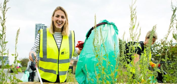 A young woman looks to the camera as she holds a litter picker and rubbish bag