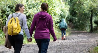 A female couple walk hand in hand through a forest as a small boy runs ahead