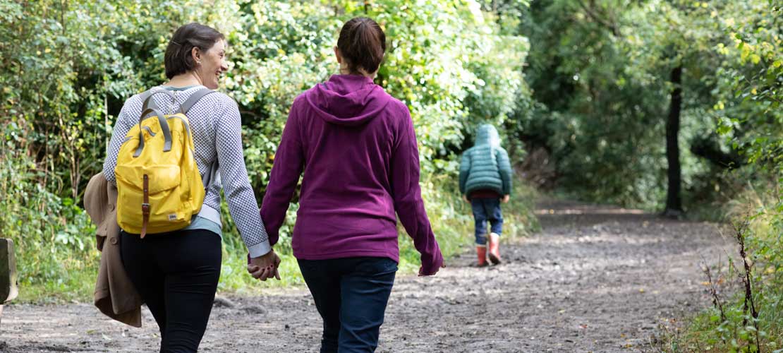 A female couple walk hand in hand through a forest as a small boy runs ahead