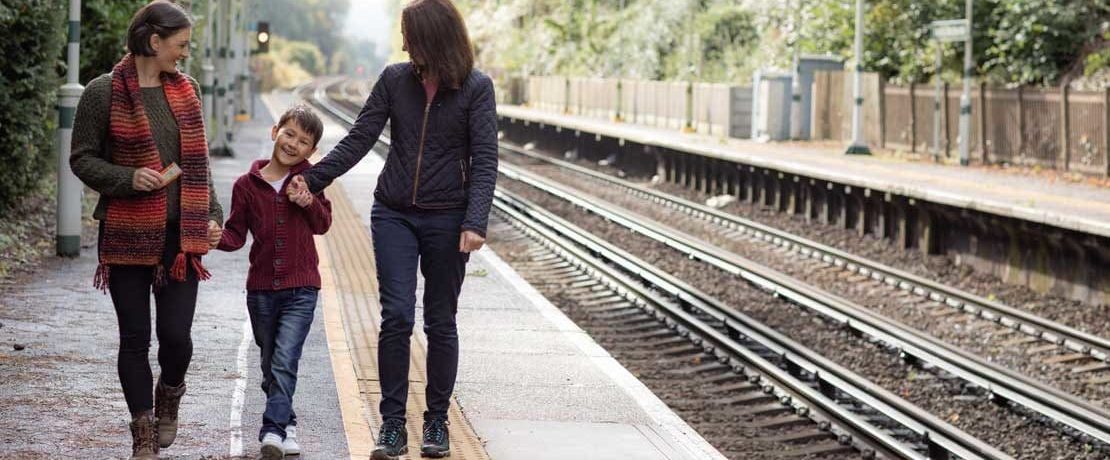 A female couple hold hands with a small child on a rural train platform
