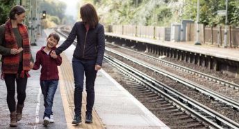 A female couple hold hands with a small child on a rural train platform