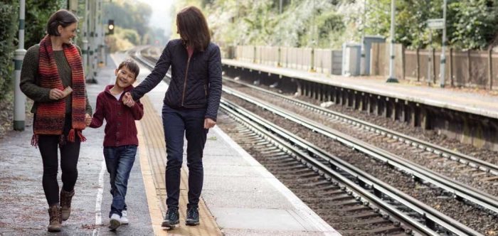 A female couple hold hands with a small child on a rural train platform