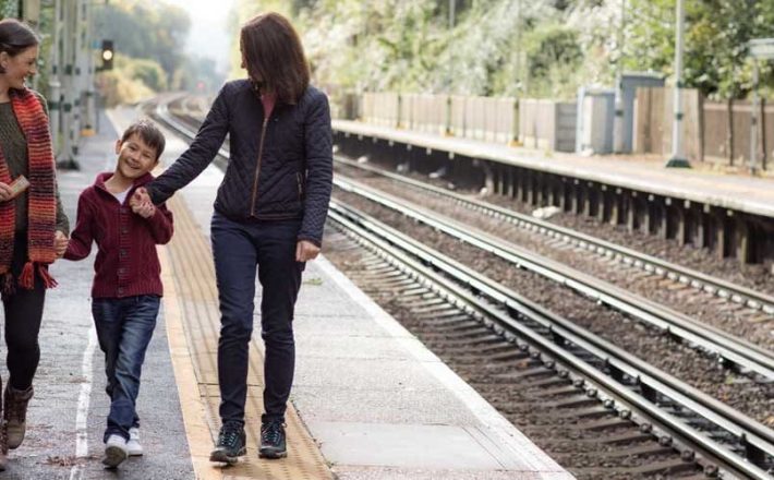 A female couple hold hands with a small child on a rural train platform