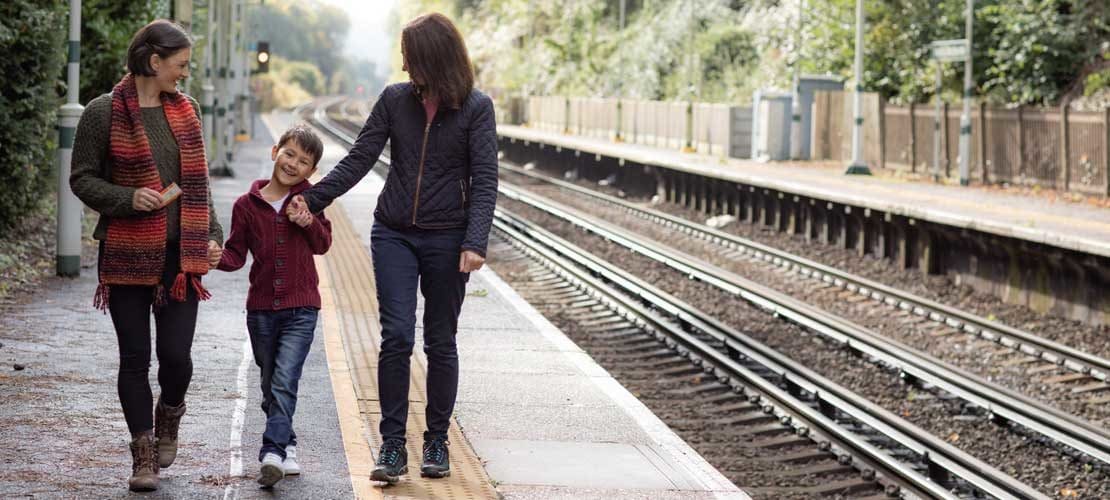 A female couple hold hands with a small child on a rural train platform