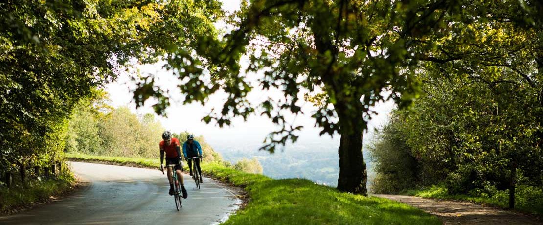 Two cyclists in lycra round a dramatic hilltop corner on a country road