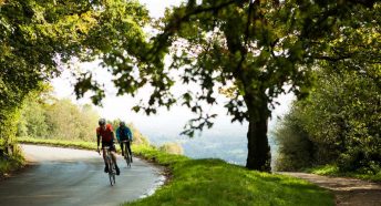 Two cyclists in lycra round a dramatic hilltop corner on a country road