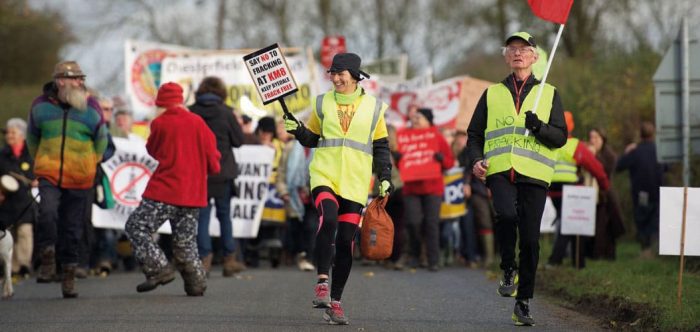 Protesters at Kirby Misperton walk along a road holding banners and wearing high-vis jackets
