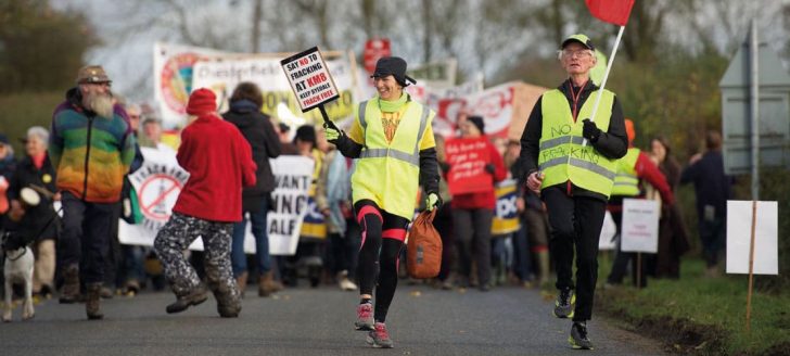Protesters at Kirby Misperton walk along a road holding banners and wearing high-vis jackets