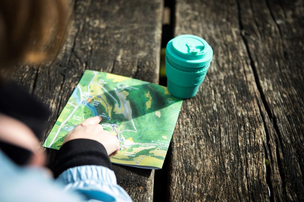 A close-up shot of a map and coffee cup on a picnic table, with someone's finger on the map