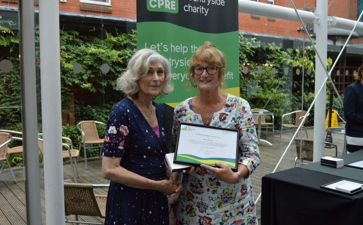 Two women shake hands as one is handed a framed certificate