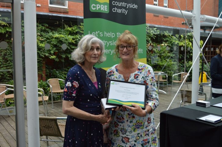 Two women shake hands as one is handed a framed certificate