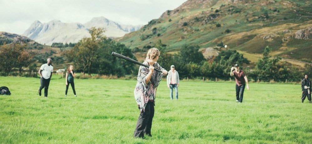 People playing rounders with large hills behind