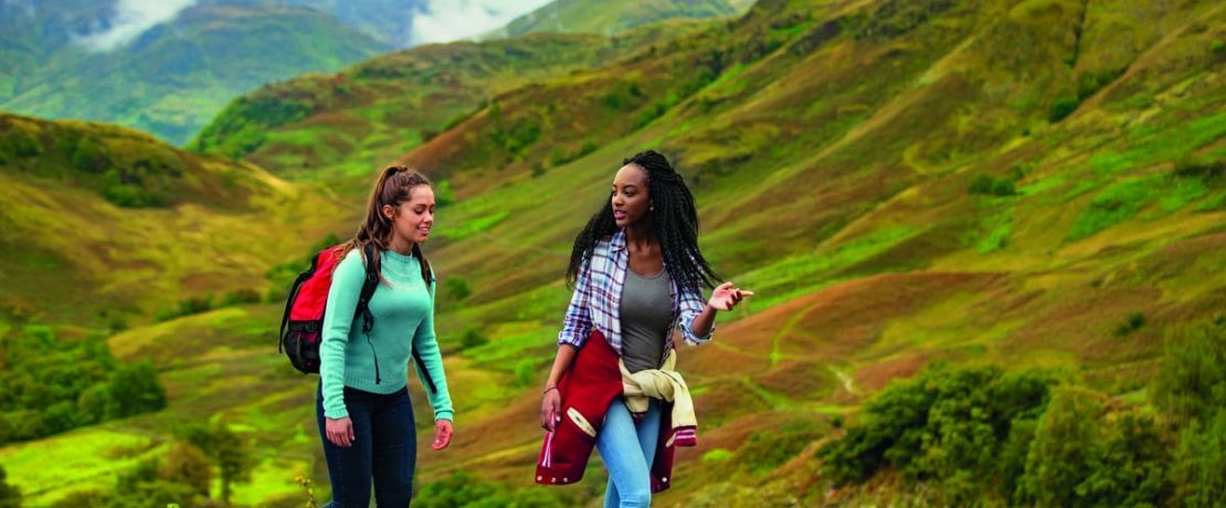 Two girls hiking through the Lake District against bright green hills