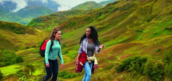 Two girls hiking through the Lake District against bright green hills