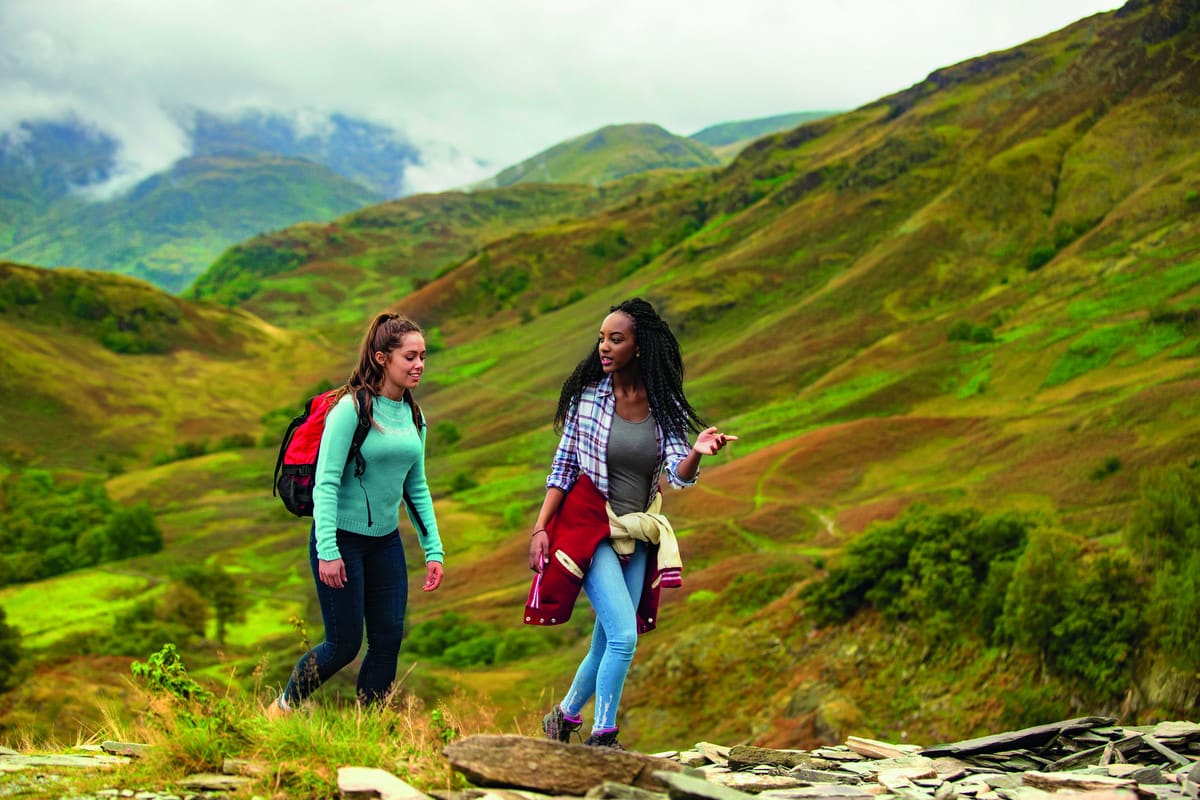Two girls hiking through the Lake District against bright green hills
