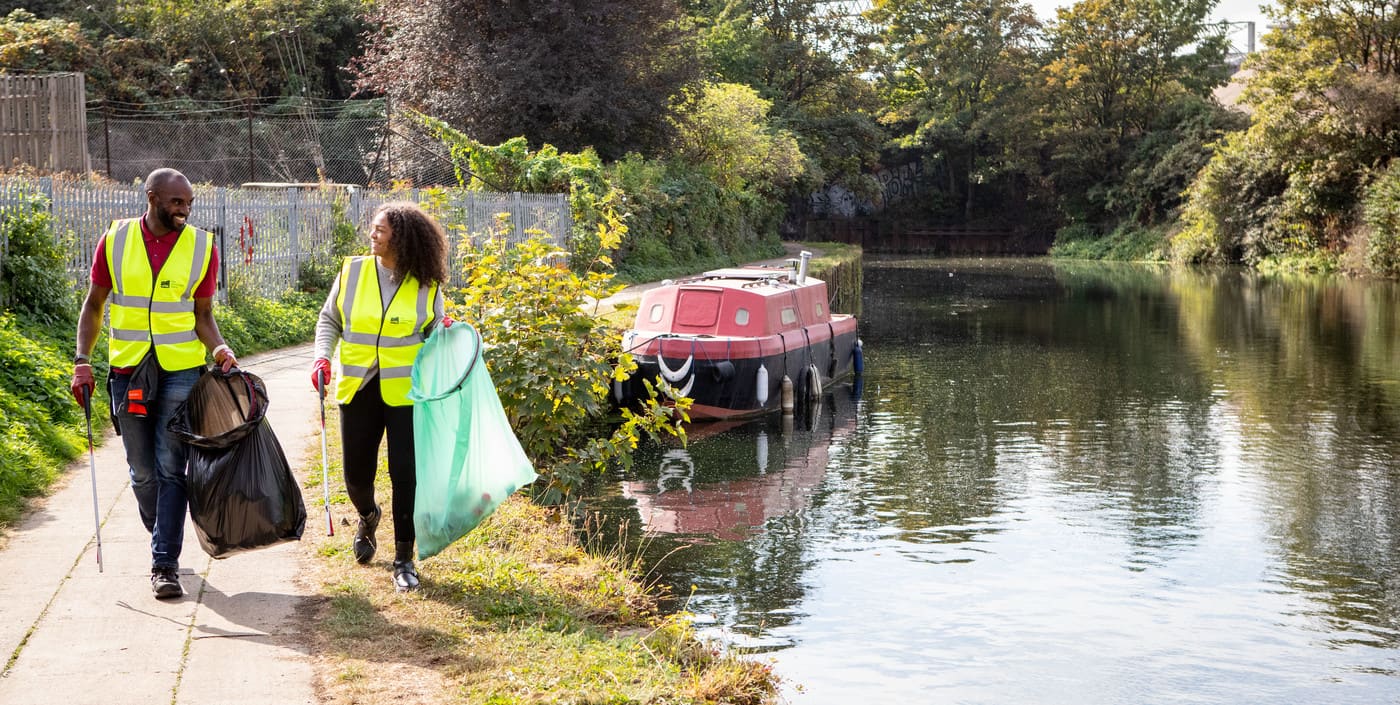 A man and woman walking as they litter pick beside a canal