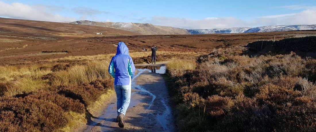 Two young people walk through a dramatic landscape with a snowy hill in the background