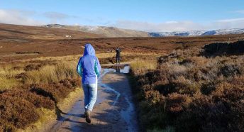 Two young people walk through a dramatic landscape with a snowy hill in the background