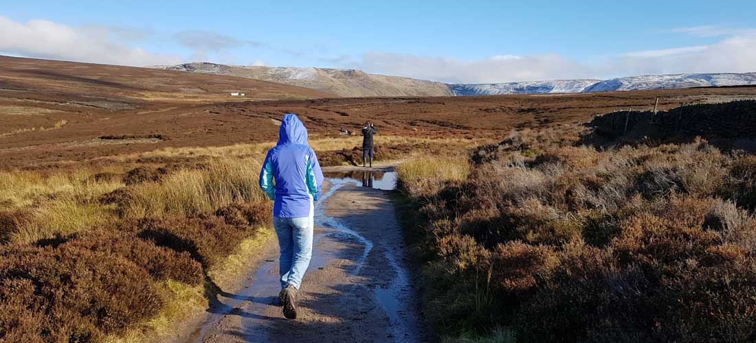 Two young people walk through a dramatic landscape with a snowy hill in the background