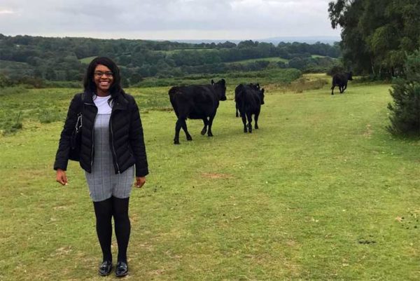 Ketsia Tampo, CPRE apprentice, stands in a grassy field near some cows