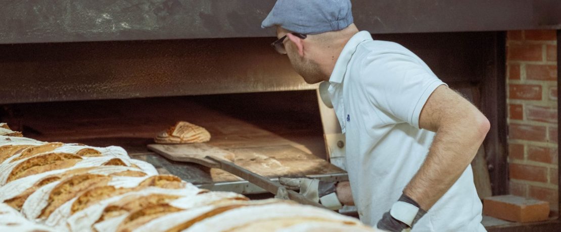 A baker lowers a loaf of bread into a large oven