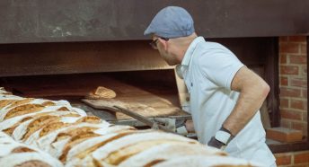 A baker lowers a loaf of bread into a large oven