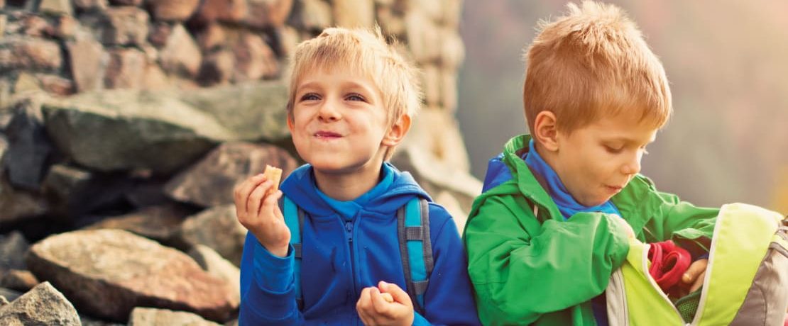 Two small boys eat lunch while sitting on rocks