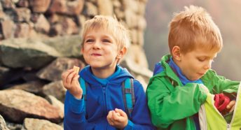 Two small boys eat lunch while sitting on rocks