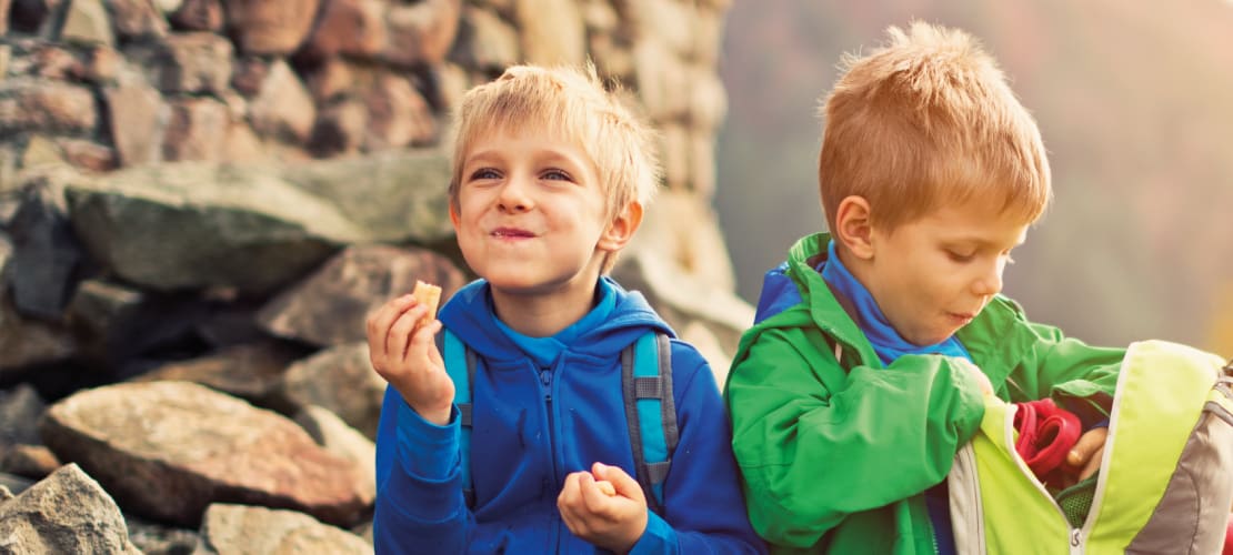 Two small boys eat lunch while sitting on rocks