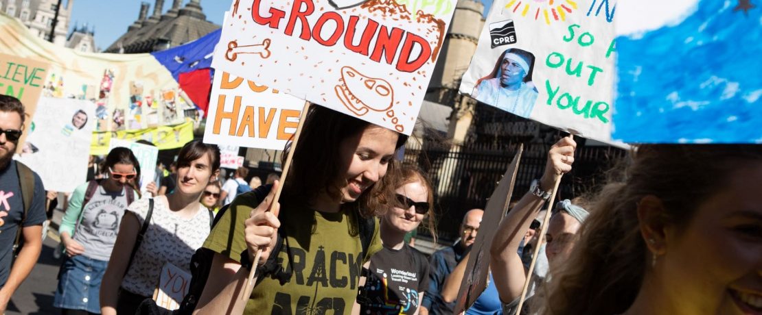 A young woman wearing a 'Frack No' t-shirt holds a banner in a protest march