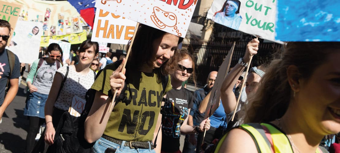 A young woman wearing a 'Frack No' t-shirt holds a banner in a protest march